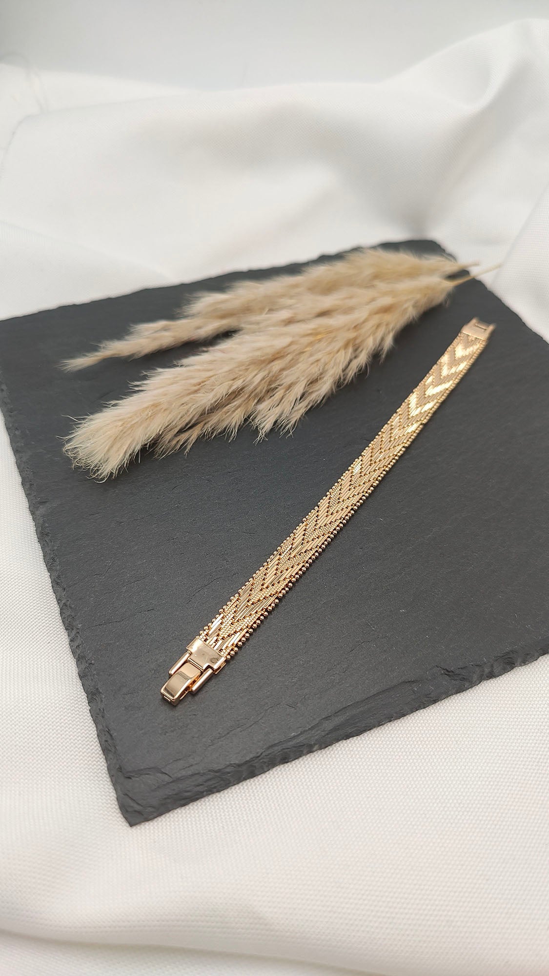 Elena Intricate Woven Bracelet with a polished gold-tone finish, featuring a delicate, intricately woven pattern on a sleek slate background.