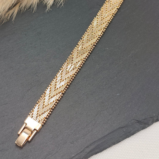Elena Intricate Woven Bracelet with a polished gold-tone finish, featuring a delicate, intricately woven pattern on a sleek slate background.