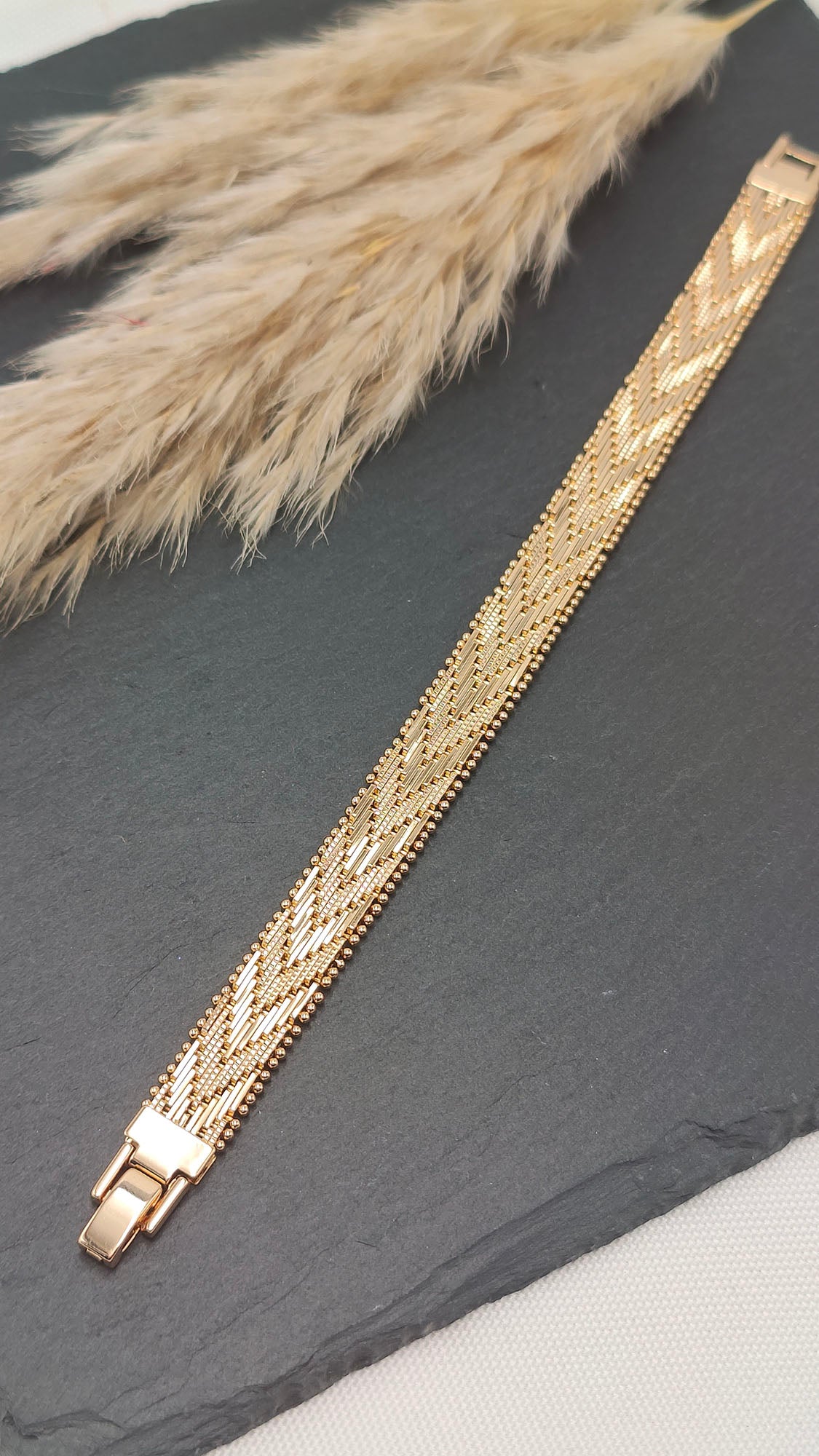 Elena Intricate Woven Bracelet with a polished gold-tone finish, featuring a delicate, intricately woven pattern on a sleek slate background.