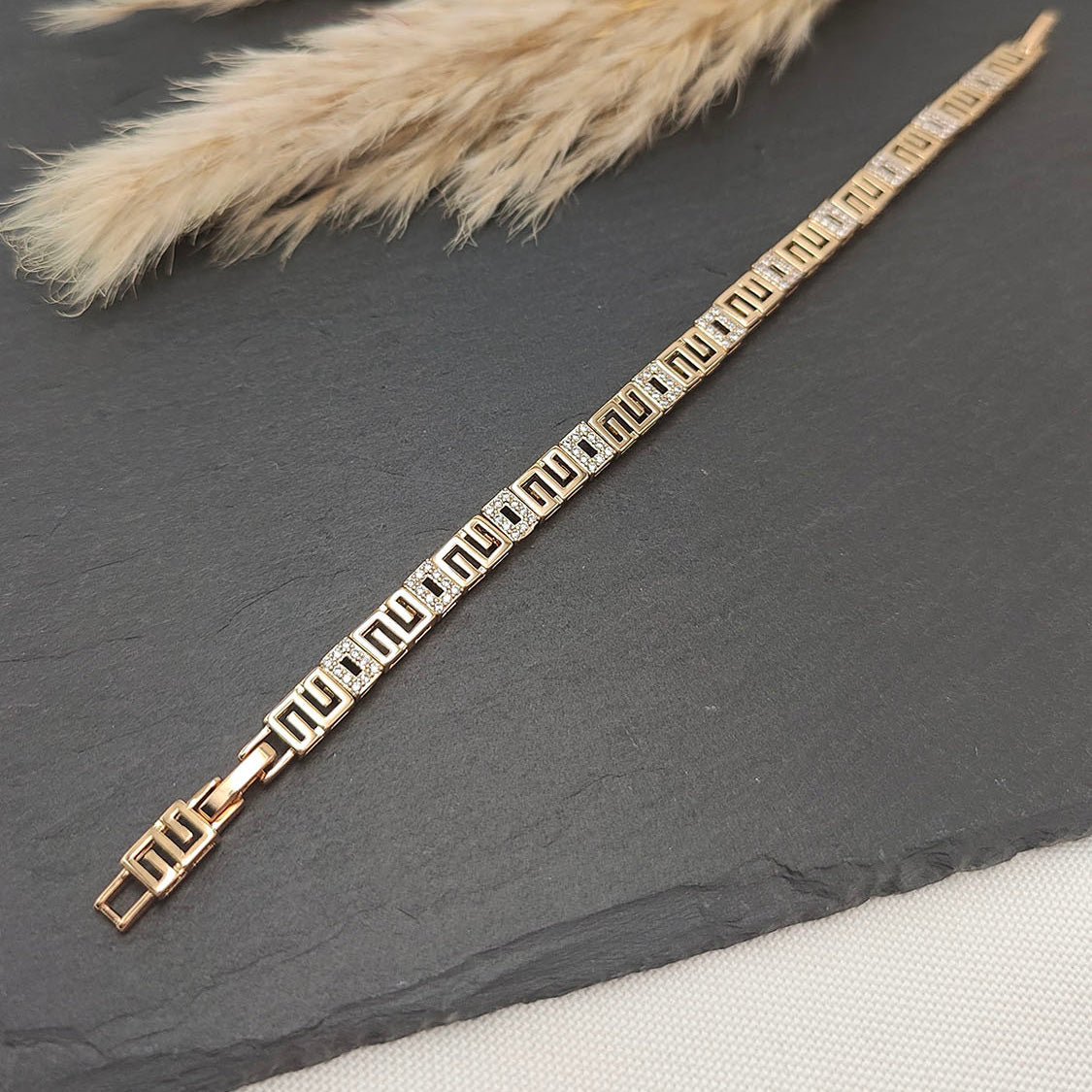 Nora Geometric Link Bracelet featuring a gold-tone geometric pattern with sparkling accents, displayed on a sleek slate background.