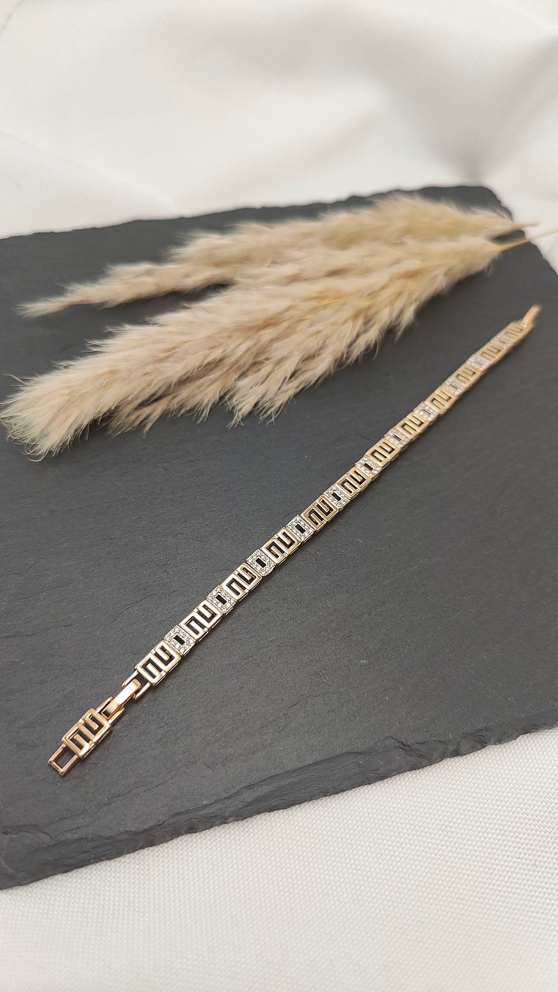 Nora Geometric Link Bracelet featuring a gold-tone geometric pattern with sparkling accents, displayed on a sleek slate background.